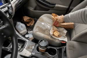 image of a car with stains and food on the car seat as the driver reaches in a bag to get more food.