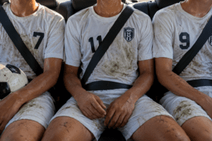 image of three soccer players that are sweaty and dirty sitting in the rear seat wearing their seat belt