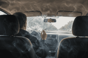 an image from a back seat passenger perspective of a driver smoking a cigarette while driving.